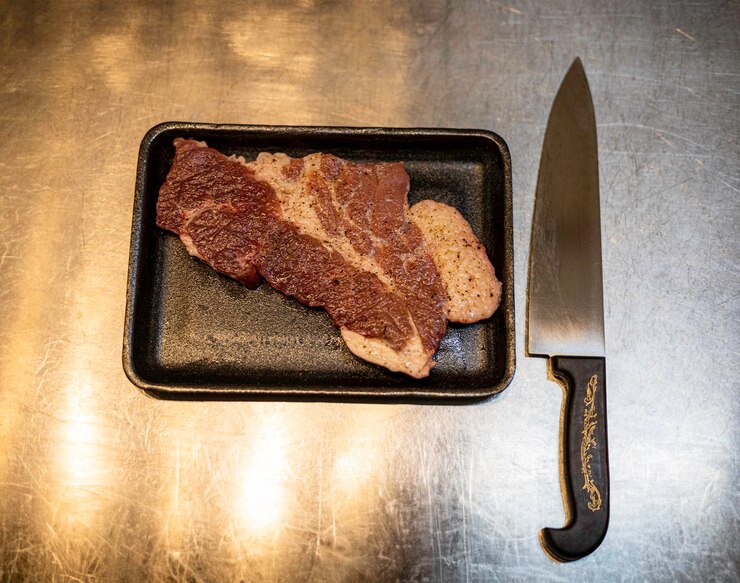 Foto faca e carne no fundo da mesa da cozinha para propaganda na cena culinária e alimentar