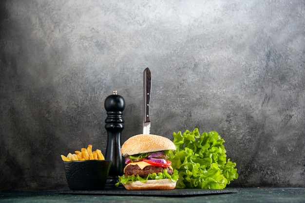 Faca em um delicioso sanduíche de carne e batatas fritas verdes na bandeja preta sobre superfície clara escura