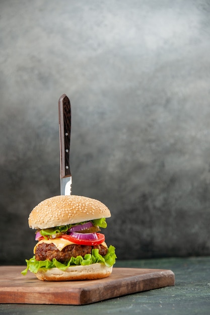 Faca em um delicioso sanduíche de carne em uma tábua de madeira em uma superfície escura isolada