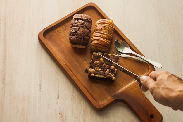 Faca na mão pronta fatia brownie de padaria na bandeja de madeira