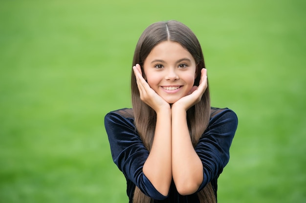 Faça sua pele brilhar. Garota feliz sorri grama verde. Saúde da pele. Dermatologia Pediátrica. Cuidados com a pele naturais. Salão de beleza. Toque seu rosto quando suas mãos estiverem limpas.