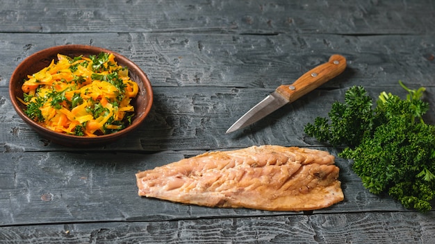 Faca, tigela com legumes no vapor e um filé de cavala em uma mesa de madeira.