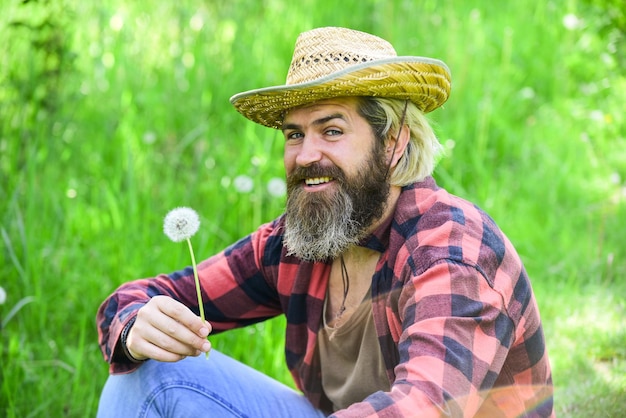 Faça um desejo Homem pacífico com chapéu de palha de verão Homem barbudo soprando sementes de dente de leão no parque Saúde mental Cara pacífico soprando dente de leão Vida feliz e despreocupada Paz de espírito Descanse e relaxe