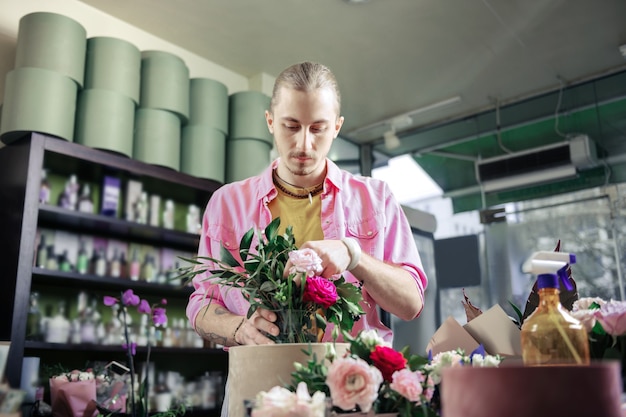 Faça uma composição. Florista séria curvando a cabeça enquanto olha rosas frescas