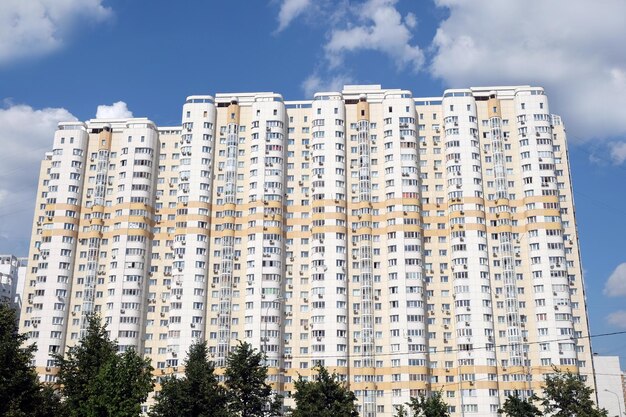 Facada de um alto edifício residencial beige moderno no céu azul com nuvens brancas