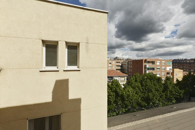 Fachada de una casa con una pared clara, pequeñas ventanas de aluminio blanco y nubes con lluvia