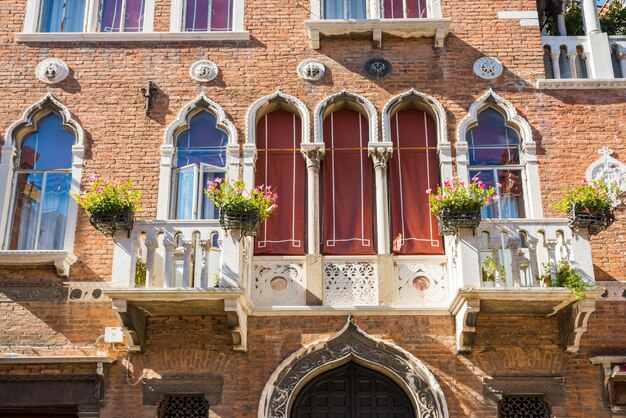 Fachada de edificio antiguo con ventanas típicas venecianas y balcón blanco con macetas Venecia Italia