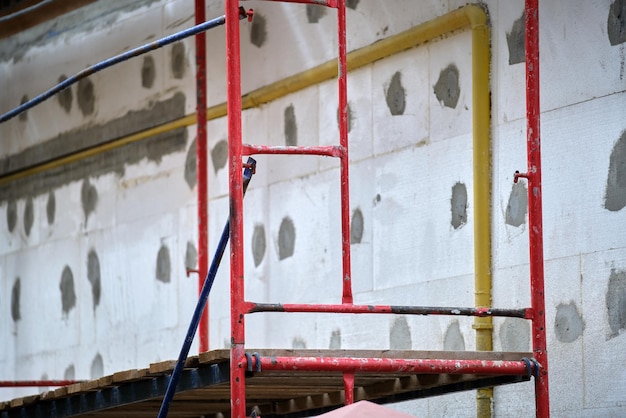 Fachada de edificio en obras de renovación con estructura de andamios de construcción. Aislamiento de paredes con láminas de espuma de poliestireno para un hogar energéticamente eficiente.