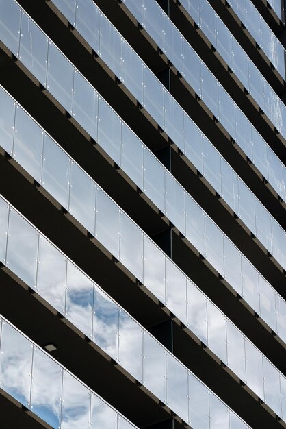 Foto fachada de un edificio residencial moderno tiras de balcón simétricas que reflejan el cielo azul