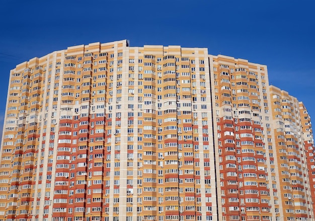 La fachada de un gran bloque de pisos de varios pisos con muchas ventanas sobre la vista frontal del cielo azul sin nubes