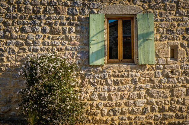 Fachada de piedra de la casa antigua con una ventana con contraventanas verdes en boucieu le roi en ardeche (francia)