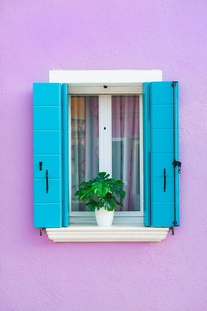 Fachada pintada de lavanda de la casa y ventana con persianas azules