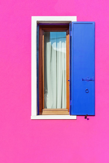 Fachada pintada de rosa de la casa y ventana con persianas azules Burano Venecia Italia