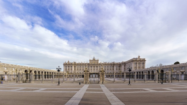 Fachada principal del palacio real de Madrid con su enorme explanada y cielo azul con nubes al amanecer. España.