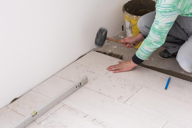 Facharbeiter beim Verlegen der Keramikfliesen in Holzoptik auf dem Boden Arbeiter bei der Herstellung von Laminatböden auf der Baustelle der neuen Wohnung