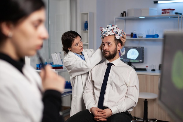 Fachforscherin, die ein eeg-Headset auf einen Patienten setzt, der die Gehirnentwicklung analysiert und die Aktivität des Nervensystems im Neurologielabor überwacht. Doktor der Neurowissenschaften, der medizinische Tomographie macht