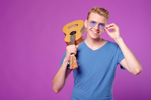 Fachion belleza hombre divertido con ukelele en manos sobre fondo púrpura copyspace