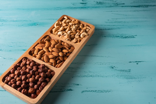 Foto fachschale mit nüssen auf blauem holztisch. cashew, haselnuss, mandel.