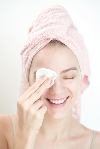 Facials. Menina com toalha no lenço de cabeça limpa a pele com uma esponja no fundo branco