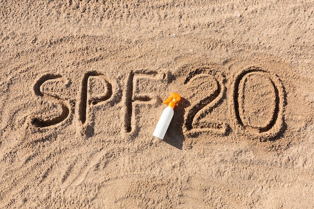 Factor de protección solar veinte SPF 20 palabra escrita en la arena y botella blanca con crema bronceadora Antecedentes del concepto de cuidado de la piel