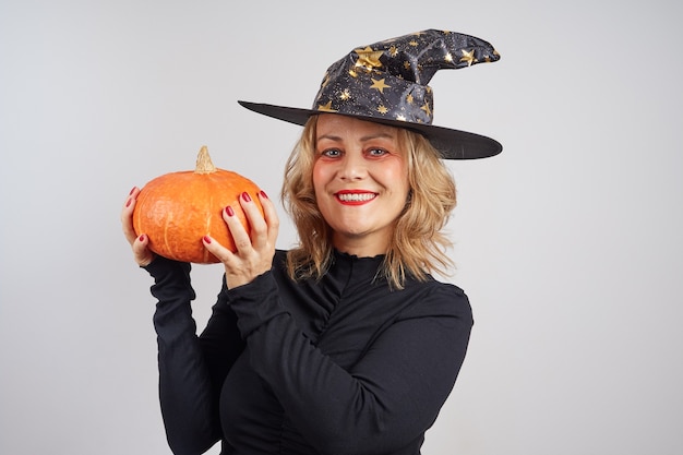 Foto fada sorridente de chapéu preto segurando uma abóbora e se preparando para o feriado de halloween