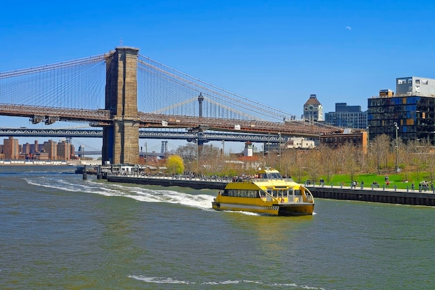 Fähre an der Brooklyn Bridge und Manhattan Bridge über den East River. Touristen an Bord. Brücken verbinden Lower Manhattan mit Brooklyn in New York, USA. Blick auf die Brooklyn-Seite.