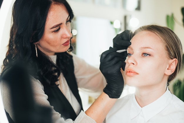 Färben und Formen von Augenbrauen. Mädchen in einem Schönheitssalon. Augenbrauen mit einer Pinzette zupfen