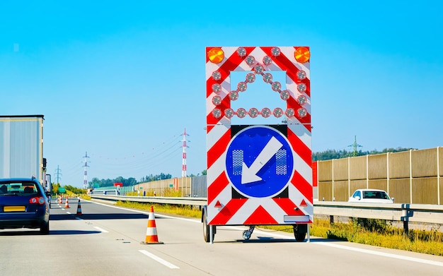 Fahrbahn- und LKW-Auto mit Verkehrszeichenanzeige während der Straßenarbeiten. Straßenurlaubsreise auf der Autobahn. Bauarbeitsbrett während der Fahrt. Bewegungsfahrt. Für den Transport. Linke und rechte Spur.