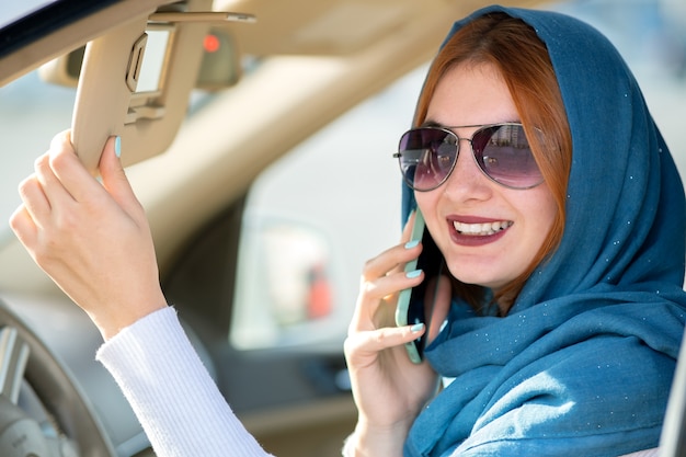 Fahrer der modernen Frau im Schal und in der Sonnenbrille sprechend am Handy beim Autofahren.