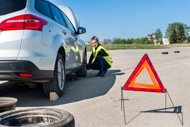 Fahrerin, die beschädigtes Rad am Straßenrand wechselt