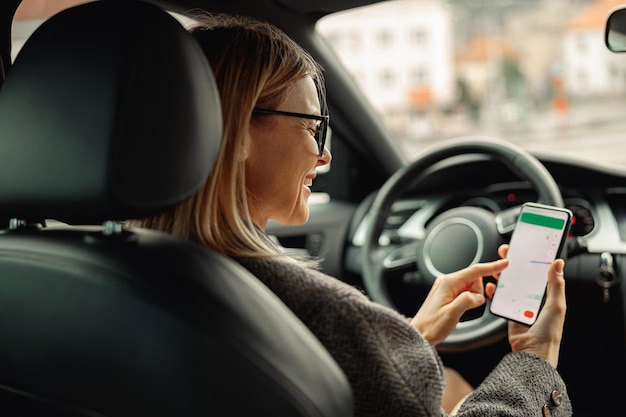 Fahrerin in Brille mit Telefon mit GPS-Navigations-App auf dem Bildschirm während der Fahrt mit dem Auto