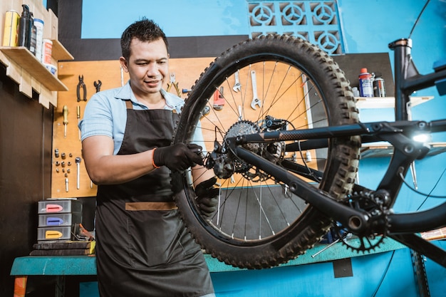 Fahrradmechaniker in Schürzen zieht Speichen fest, während er Probleme behebt