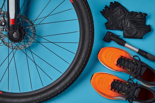 Fahrradrad, orange Turnschuhe, Pumpe und Fahrradhandschuhe auf blauem Grund. Fahrradtag