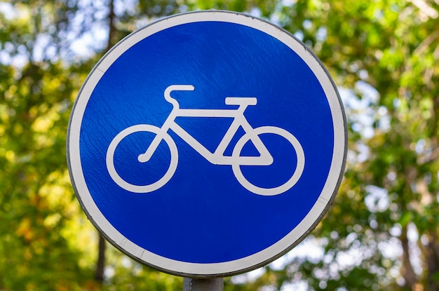 Fahrradschild auf grünem, sonnigem Laubhintergrund Blau-weißes Fahrradwegschild, das auf die Fahrradroute hinweist