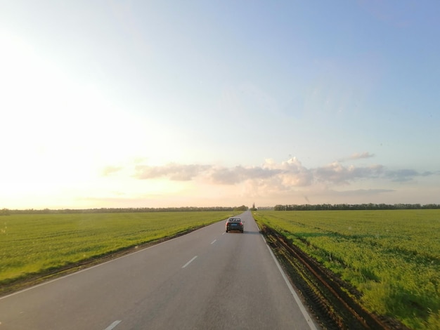 Faixa ao pôr do sol entre campos com um carro