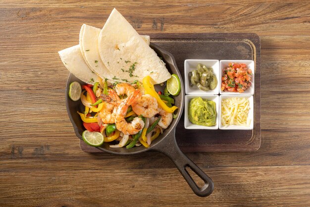 Fajita de gambas mexicanas con pimientos, verduras a la parrilla y cebollas, vista superior sobre fondo de madera oscura