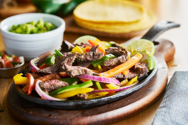 Fajitas de carne mexicana en una sartén de hierro con pimientos y guacamole al lado