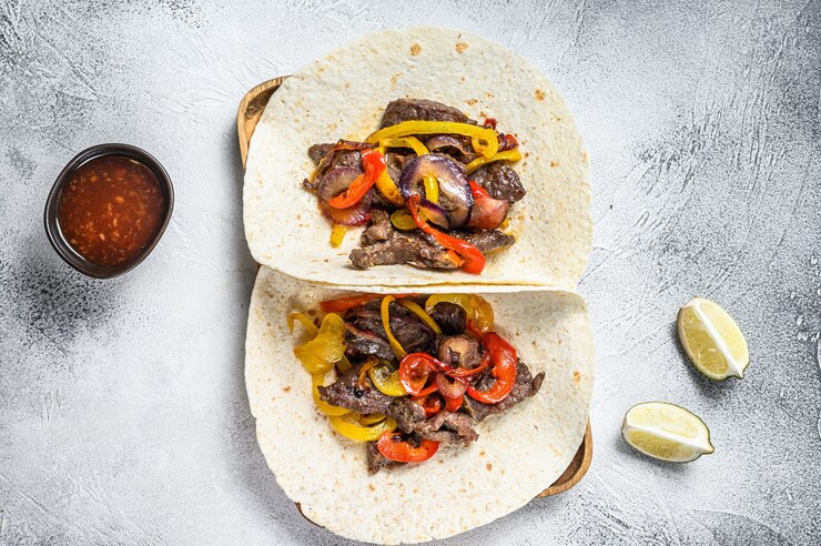 Foto fajitas com riscas de carne bovina, pimentão colorido e cebolas, servidas com tortilhas e molho. fundo branco. vista do topo.