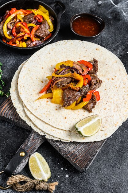 Fajitas de filete de res con tortilla, mezcla de pimiento y cebolla comida tradicional mexicana. Fondo negro. Vista superior.