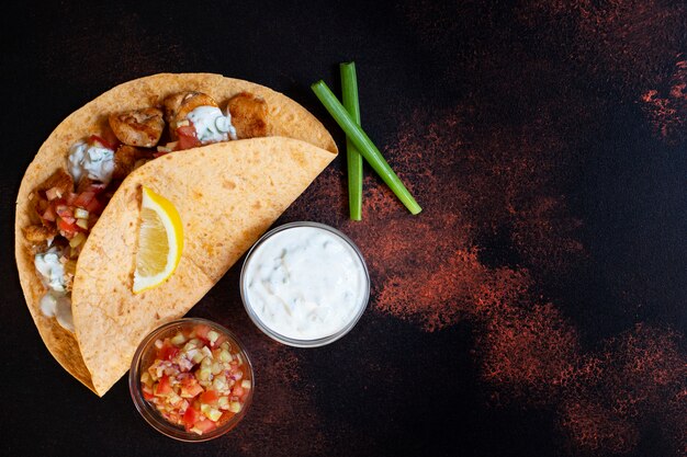 Fajitas mexicanas tradicionales con pollo y verduras, servidas en tortilla con salsa blanca y roja, limón y cebolla verde fresca. Vista superior. fondo oscuro Copia espacio