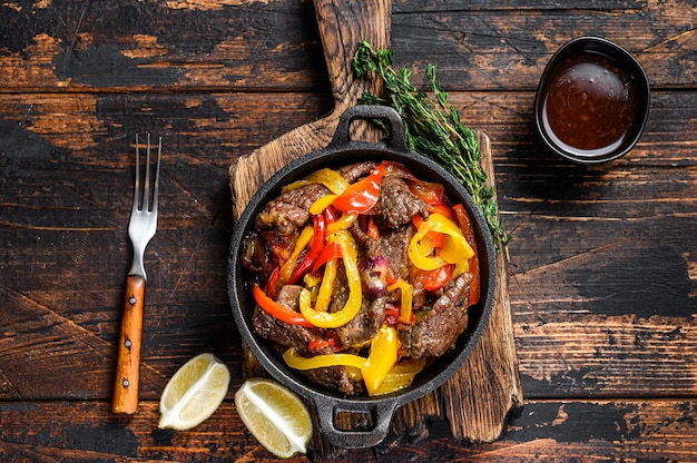 Fajitas Rindfleisch Fleisch traditionelles mexikanisches Gericht in einer Pfanne. Dunkler hölzerner Hintergrund. Draufsicht.