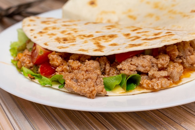 Fajitos con verduras de carne picada en una tortilla de maíz sobre una placa azul fondo de madera oscura. concepto de comida tradicional de comida rápida