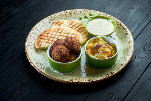 Falafel con pan de pita, servido con salsa blanca y encurtidos en un plato verde Comida vegetariana