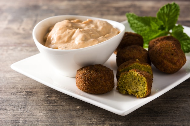 Falafel en un plato y salsa de tahini en mesa de madera