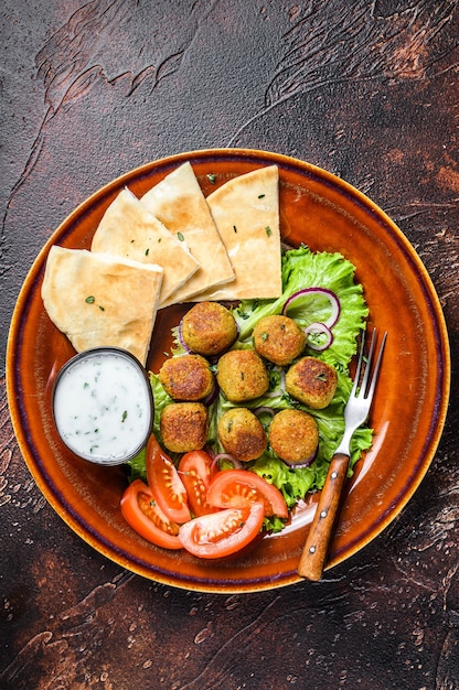 Falafel vegetariano con pan de pita, verduras frescas y salsa en un plato.