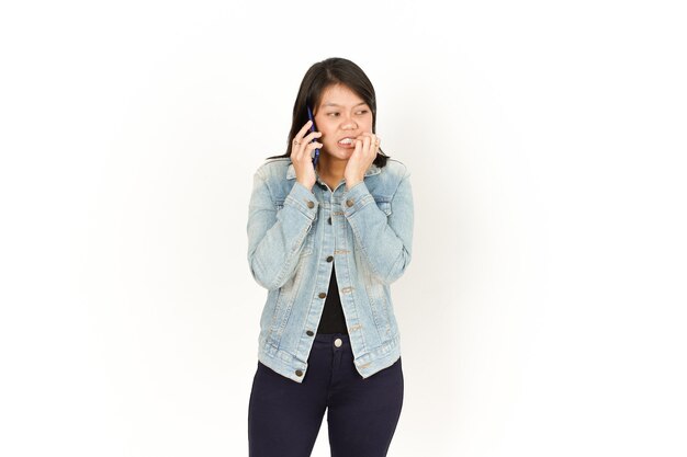 Falando ao telefone com a cara de medo de uma bela mulher asiática vestindo jaqueta jeans e camisa preta