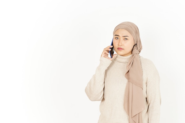 Falando ao telefone com o rosto sério de uma linda mulher asiática usando um hijab isolado no branco