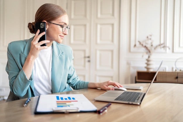 Falando ao telefone com um colega uma mulher no escritório usando um computador laptop online