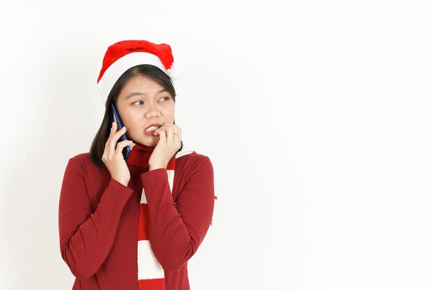 Foto falando ao telefone com uma expressão triste no rosto de uma mulher asiática com gola alta vermelha e chapéu de papai noel