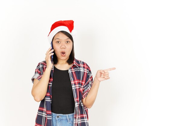 Falando ao telefone e apontando para o lado de uma mulher asiática vestindo uma camisa xadrez vermelha e um chapéu de Papai Noel